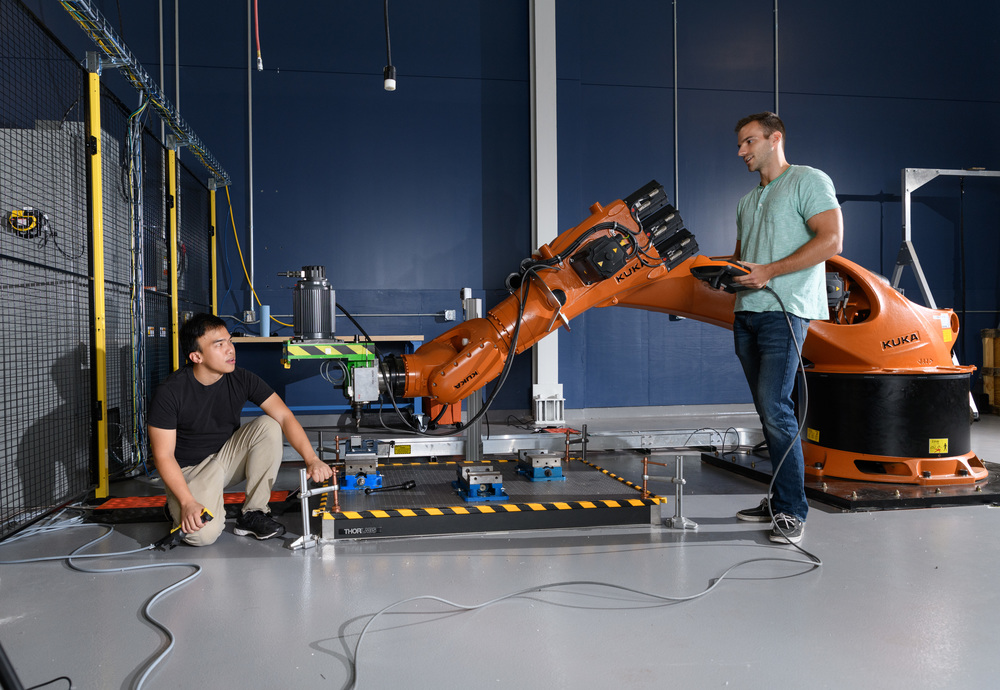 Two students with an industrial robot in the Applied Manufacturing Pilot Facility (AMPF).