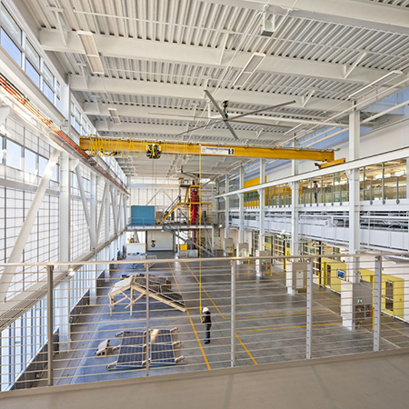 A view from the mezzanine overlooking the CNES Laboratory Building high bay space with a ceiling crane hoisting a solar array off the ground.