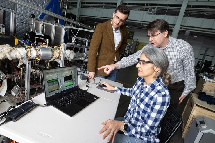Postdoctoral fellow Poorandokht Kashkouli, seated at laptop, discusses test data from their direct air capture rig. Ryan Lively, left, and Chris Jones, pointing at laptop, stand next to the rig, which is a series of tubes and valves in a metal frame. (Photo: Candler Hobbs)