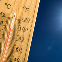 stock photo of a thermometer with a high temperature and a sunny sky behind it