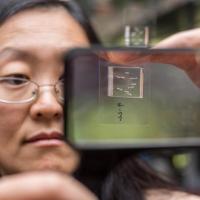 <p>Engineering Professor Hang Lu holds up a chip used to immobilize <em>C. elegans</em> roundworms for photographing by a microscope optic connected to a computer. The chip then sorts the worms into one of two channels for either mutants or non-mutants, a status an algorythm determines based on subtle phenotypical differences it recognizes in the microscope photo. Credit: Georgia Tech / Rob Felt</p>